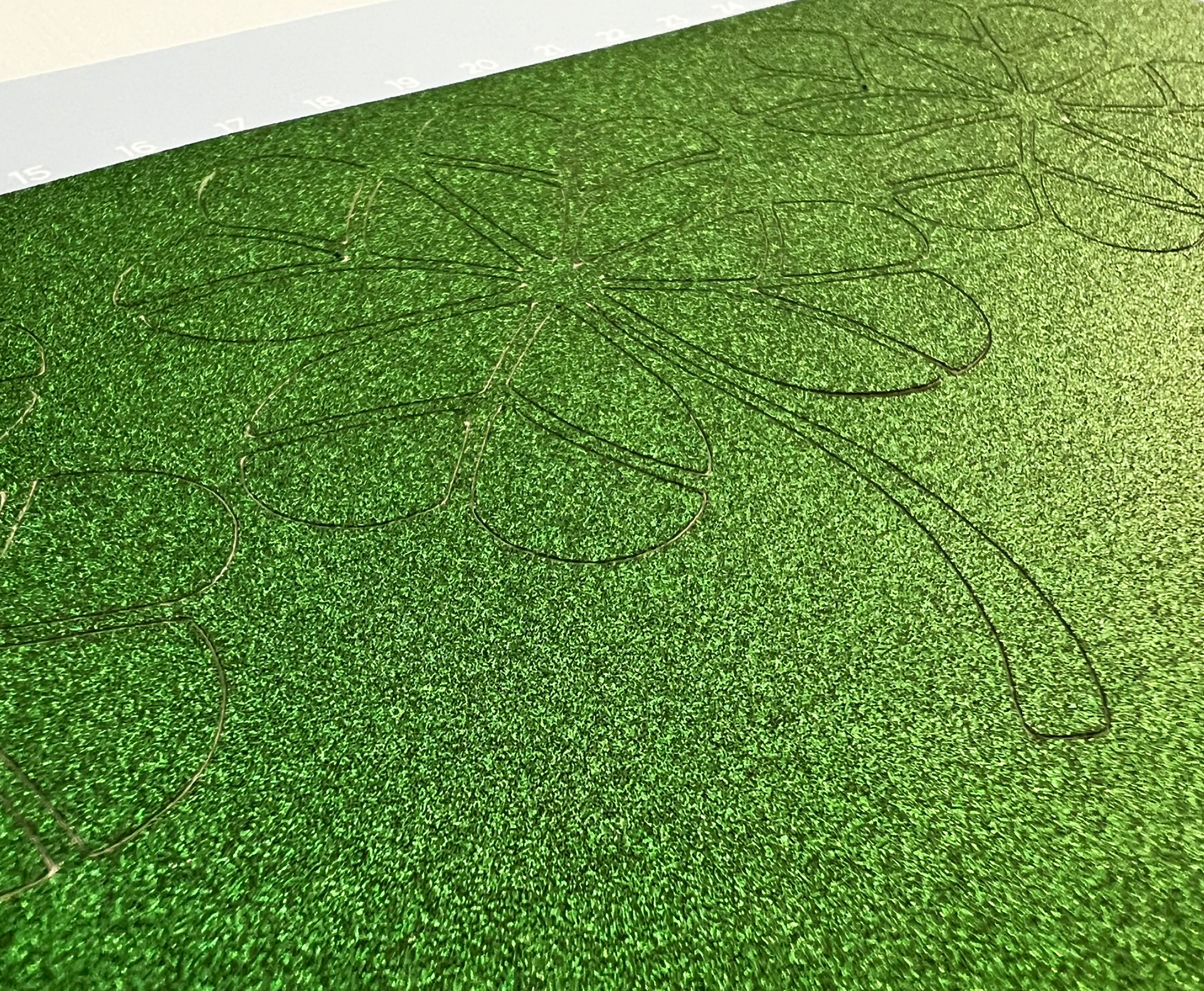 Emerald green no-shed glitter cardstock immediately after cutting, with the four-leaf clover design still embedded in the sheet before weeding.