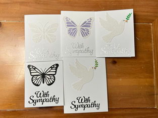 Five handmade sympathy cards with butterfly and dove designs displayed on a wooden table.