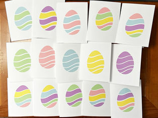 Fifteen handmade pastel Easter egg greeting cards arranged on a wooden surface