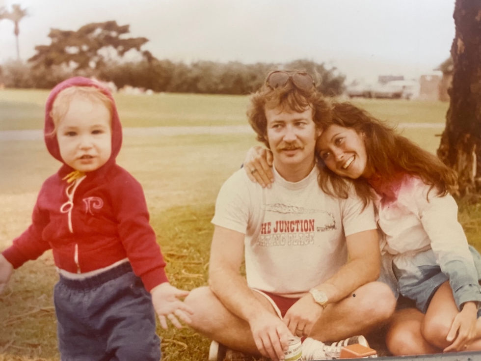 Couple with small child sitting on grass smiling. Photo was taken in early 1970s.
