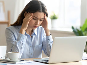 אשה יושבת ליד מחשב ומחזיקה את הראש בידיה מוטרדת
