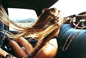 A girl's hair blows in the wind as she rides in the backseat of a car on a road trip and summer drive