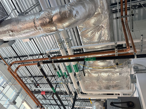 Industrial piping installation to Espec Platinum Series temperature and humidity chambers at AMD R&D Laboratory in Austin, showing elevated scissor lift access, hot tap system integration, and precision overhead piping completed under active lab conditions.