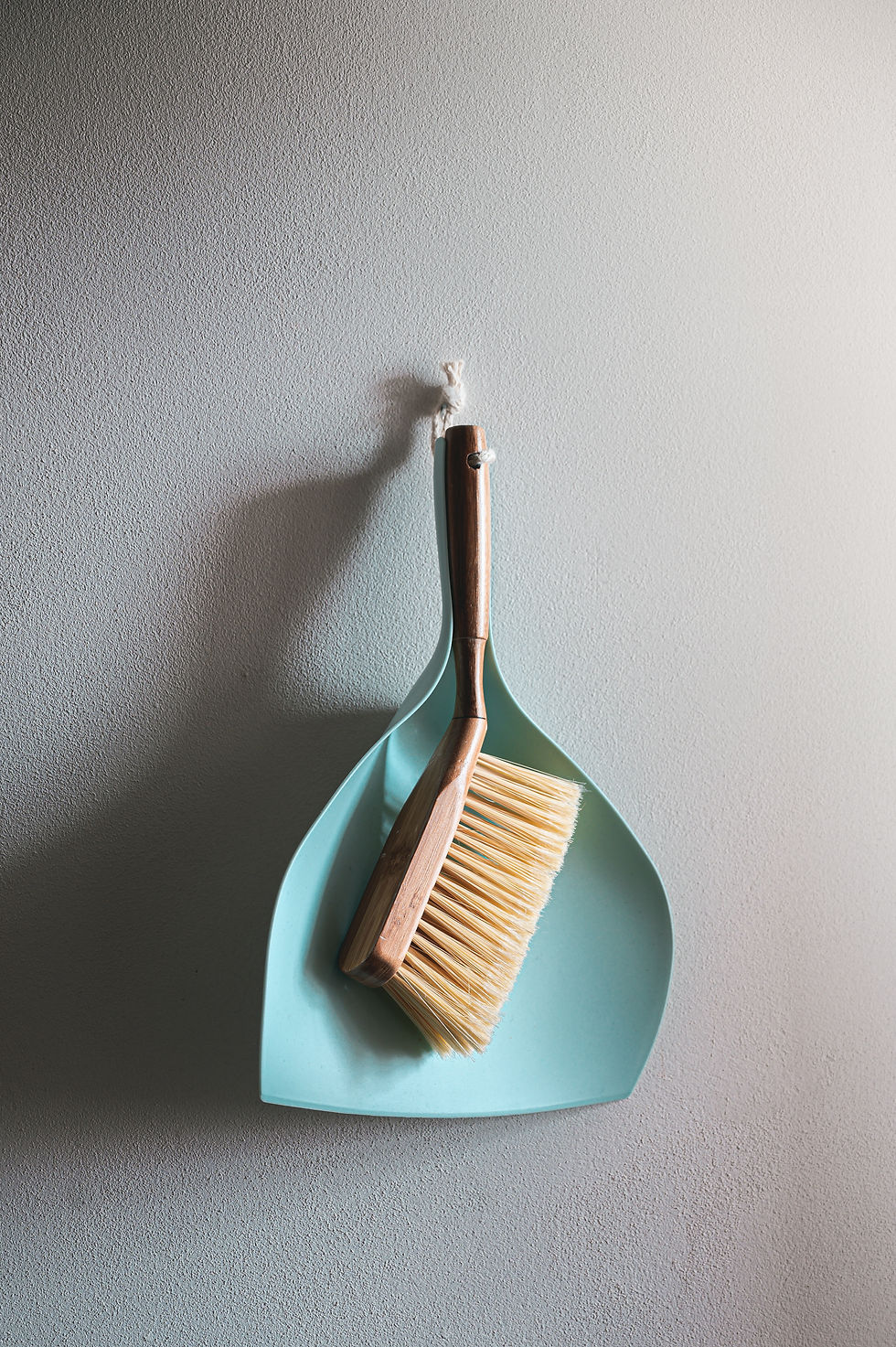 Teal dust pan and wooden brush hanging on a blank white wall