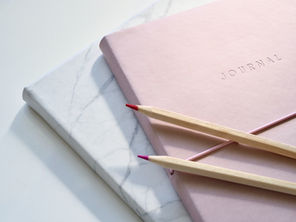 Pink journal resting on a marble-patterned book. Two wooden pencils diagonally on top representing spring journal prompts for business growth.