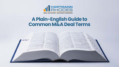 Open dictionary on a white background with text: "A Plain-English Guide to Common M&A Deal Terms" and logo "Hartmann Rhodes."