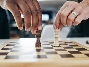 Two hands holding chess pieces—black and white kings—on a chessboard. The background is blurred, creating a focused and intense mood.