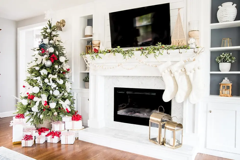 Christmas tree with red and silver ornaments, gifts below. Fireplace with white stockings, garland, and lanterns. Cozy holiday setting.