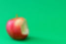 A red apple with a bite taken out, set against a bright green background. The vibrant colors create a fresh and crisp mood.