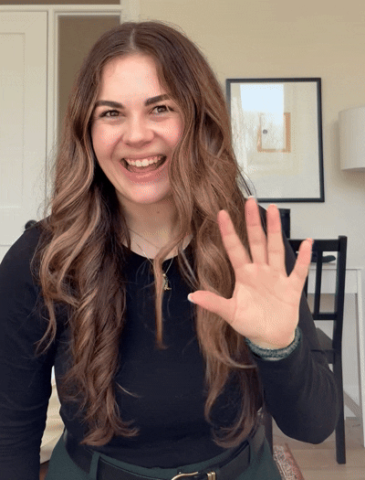 GIF image of woman with long brown hair smiling and waving 