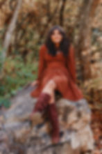 A high school senior sits on a rock among the fall foliage and smiles