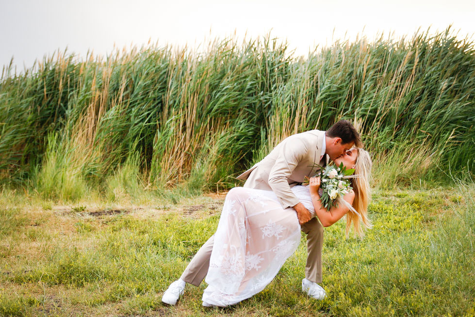 A groom dips a bride on their wedding day in a field of tall grass