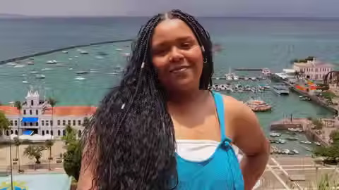 Caroline Soares, mulher negra de cabelos longos, com uma paisagem ao fundo de um lago cheio de barcos.