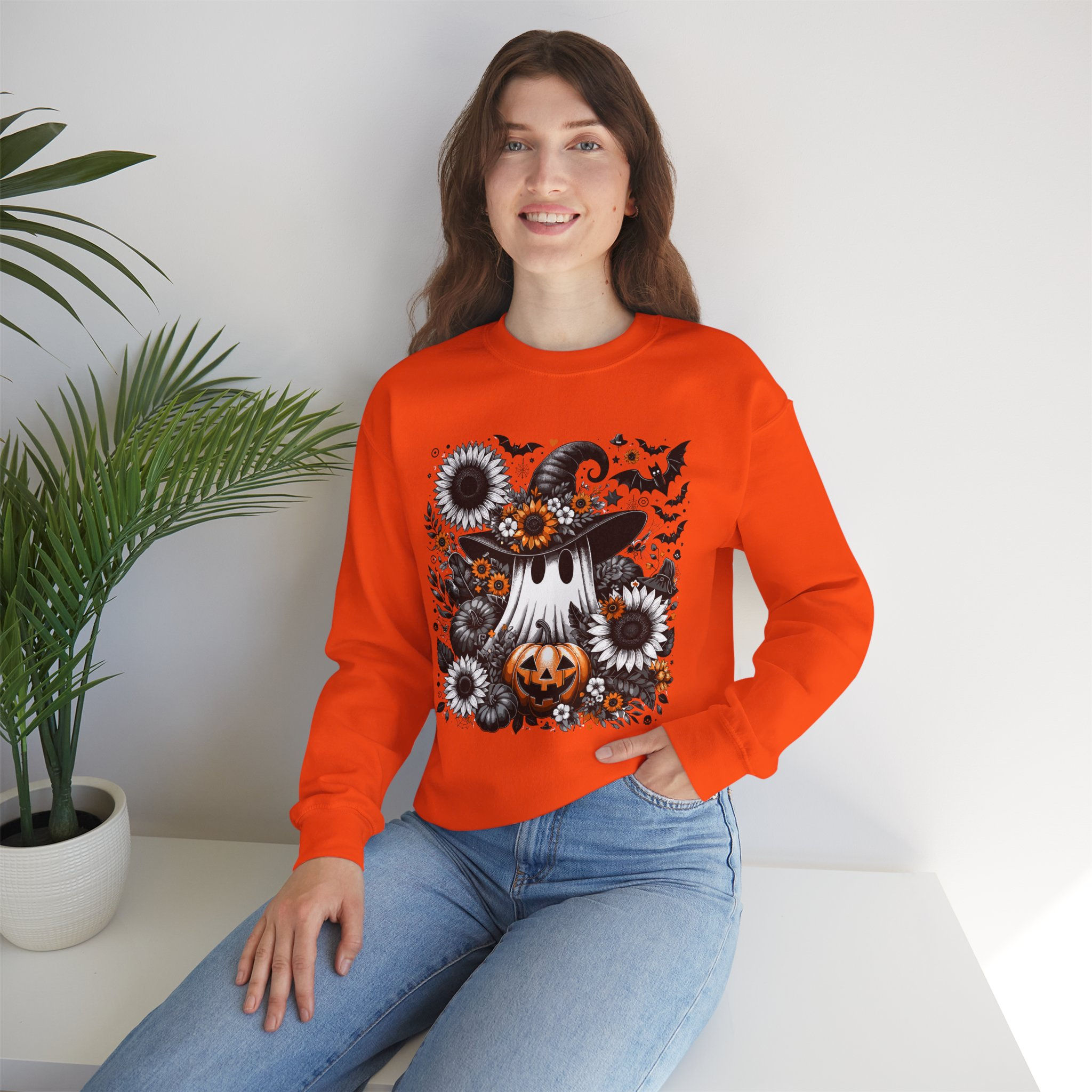 Woman wearing orange Halloween sweatshirt with graphic, sitting near plant.