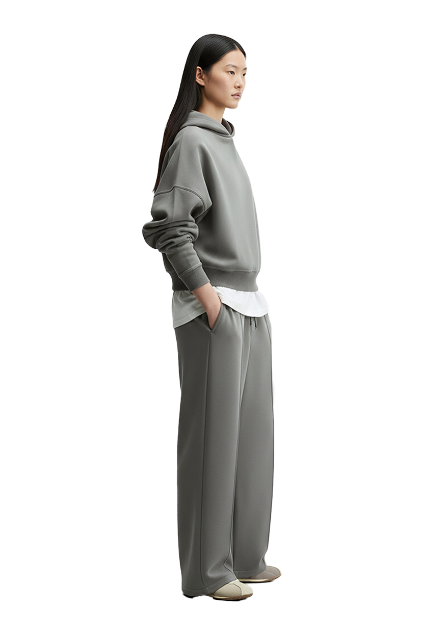Woman wearing gray hoodie and pants, Drift Layer tee, standing with neutral background.