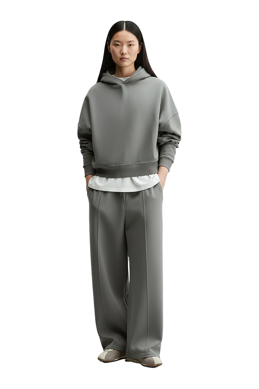Woman wearing gray hoodie, pants and Drift Layer tee, standing against a backdrop.