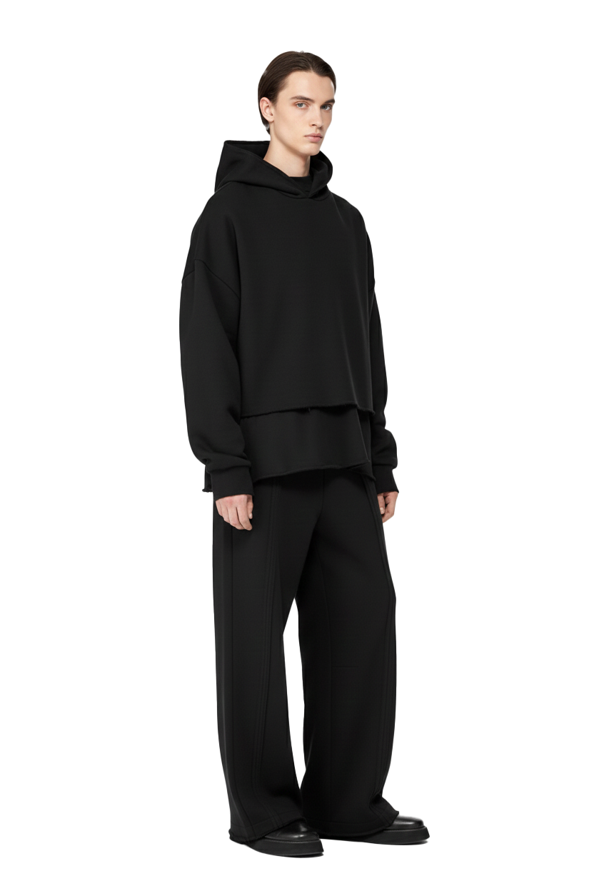 Person wearing black hoodie and pants, standing with neutral background, fashion style.