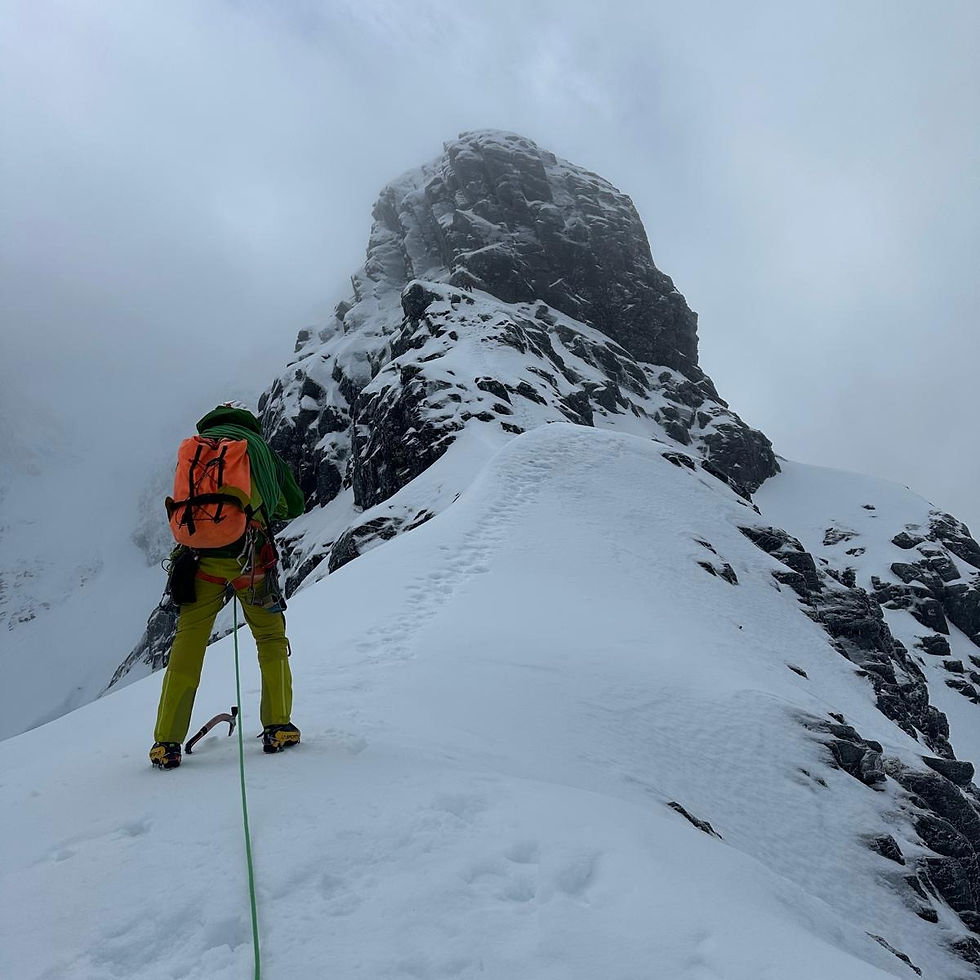 Mountaineer ascending a steep snowy slope with ice axe and climbing harness, approaching a rocky peak in misty alpine conditions