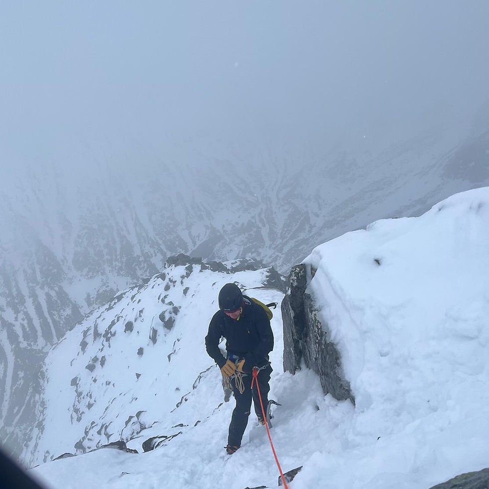 Ice climber on a snow and ice slope in heavy mist, with rocky outcrops and a deep valley barely visible through the fog
