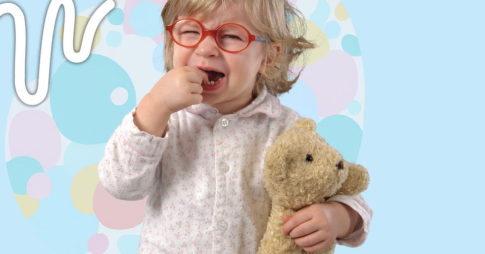 A crying toddler in red glasses holds a teddy bear against a colorful pastel backdrop with circles, wearing a light pink floral shirt.