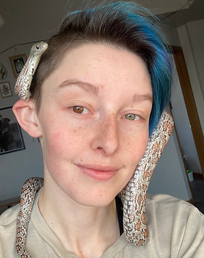 Smiling, Blue haired person with grey corn snake wrapped happily around their head and tucke on top of their ear.