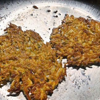 A stainless steel frying pan cooking two hash browns. They have been flipped and a crispy golden brown side is facing up.