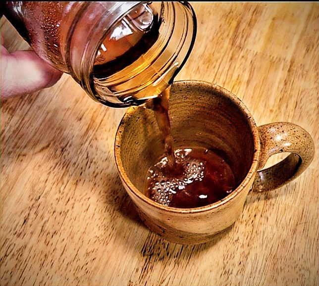 brewed London Grey tea being poured out of a glass jar and into a tea mug