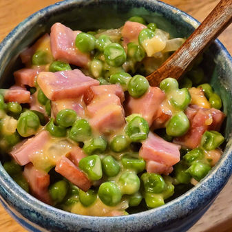 A blue pottery bowl of cheesy peas with ham