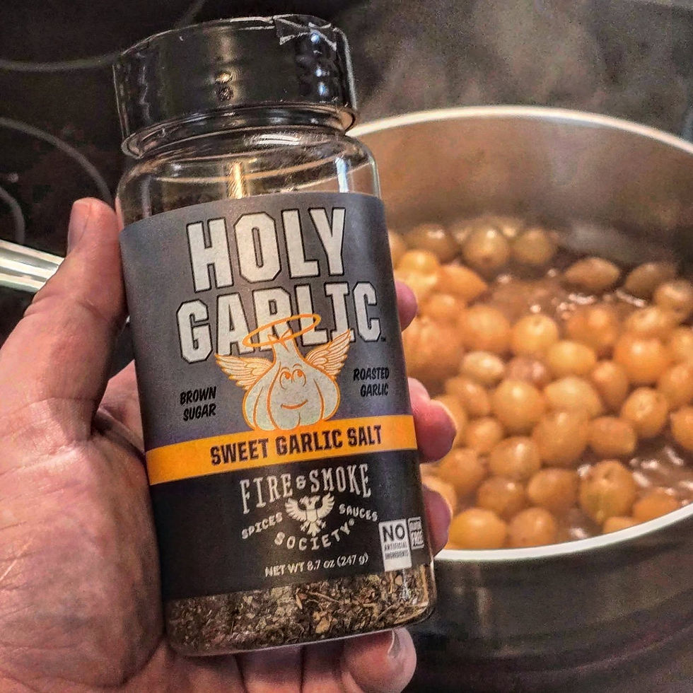 A hand is holding up a bottle of garlic salt seasoning. A stainless steel pan with braised pearl onions can be seen in the background