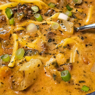 a closup picture of hamburger soup with green onions and shredded cheese as a garnish