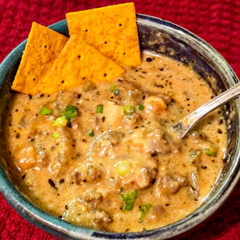 Hamburger soup in a pottery bowl garnished with crackers and green onion