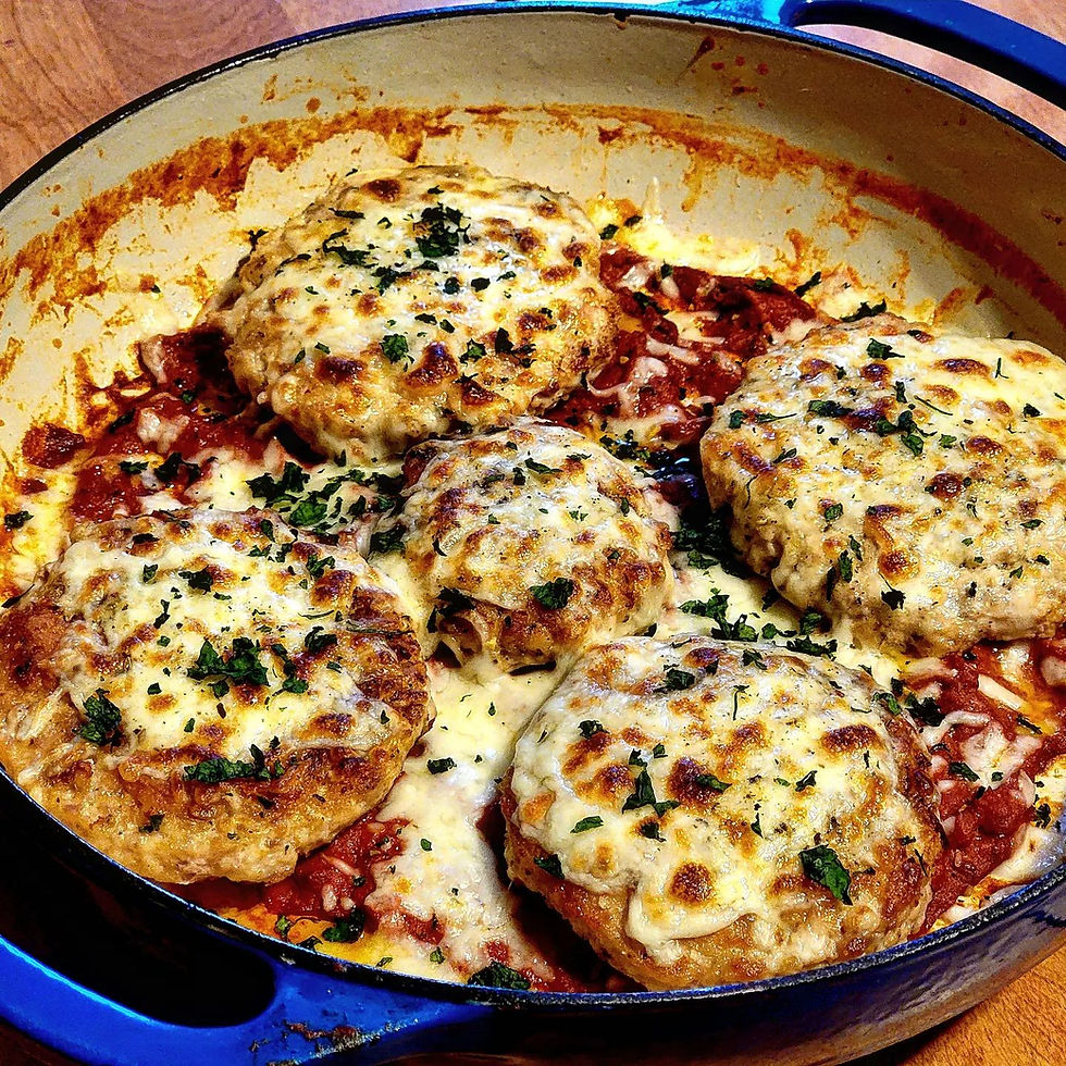 a finished pan of pesto mozzarella chicken patties with melted cheese sitting on a bed of vodka sauce reduction, sprinled with fresh basil