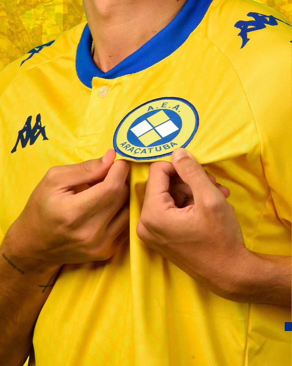 Escudo da Associação Esportiva Araçatuba em camisa amarela do clube