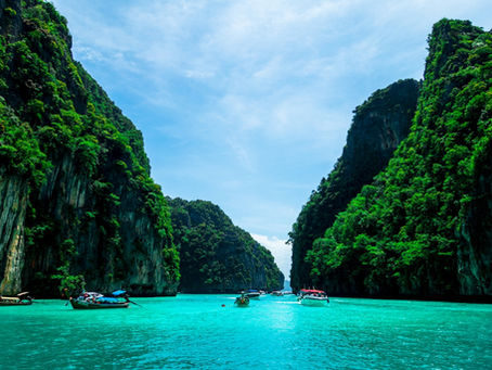 Phuket Travel Guide: Traditional Thai longtail boats and speedboats navigating the turquoise waters of Maya Bay, Phi Phi Islands, framed by towering, lush limestone cliffs.