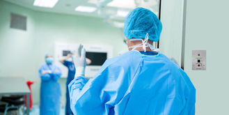 Ein Arzt in einem Krankenhaus, gekleidet in blaue OP-Kleidung und mit blauem Haarnetz, geht durch eine Tür und wedelt mit der Hand vor einem Parabit-Wellen-Schalter, um diesen berührungslosen Türöffner zu öffnen
