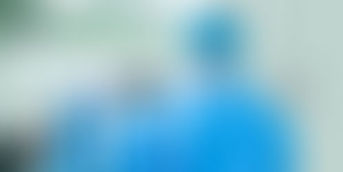 Ein Arzt in einem Krankenhaus, gekleidet in blaue OP-Kleidung und mit blauem Haarnetz, geht durch eine Tür und wedelt mit der Hand vor einem Parabit-Wellen-Schalter, um diesen berührungslosen Türöffner zu öffnen