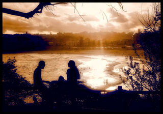 a silhouette of two people sitting on the bondi beach head 