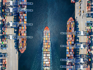 Ship passing through shipping port stacked with containers. This represents uncertainty with recent tariffs being placed.