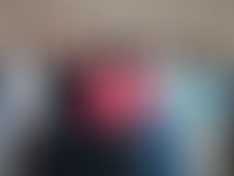 Seven women stand in a line, smiling against a beige wall. They're dressed in casual attire, with diverse patterns and colors.