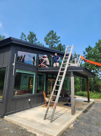 Two workers installing large windows on a dark modern home
