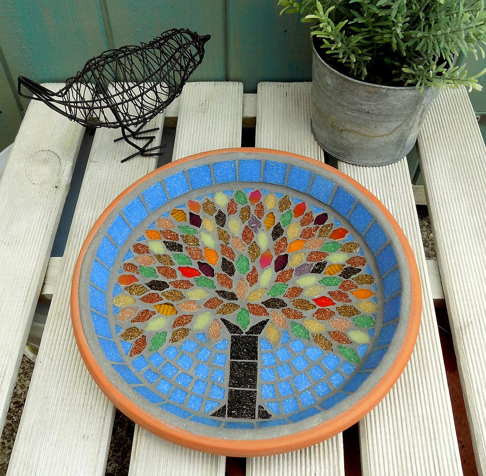 A mosaic bird bath made in a garden terracotta saucer with an autumn tree design using iridescent highlight tiles.
