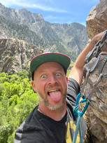 Man placing rock climbing anchors with tongue out.