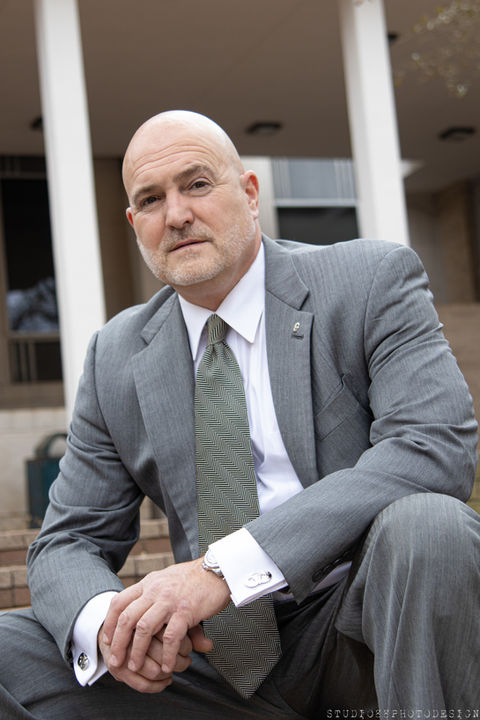 Bald man in grey suit and green tie sitting on steps