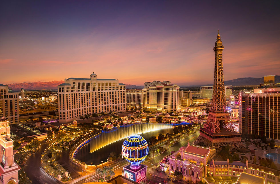 Aerial view of the Las Vegas Strip at night with the Bellagio fountains, Paris Las Vegas Eiffel Tower, and neon lights glowing against the desert sunset.