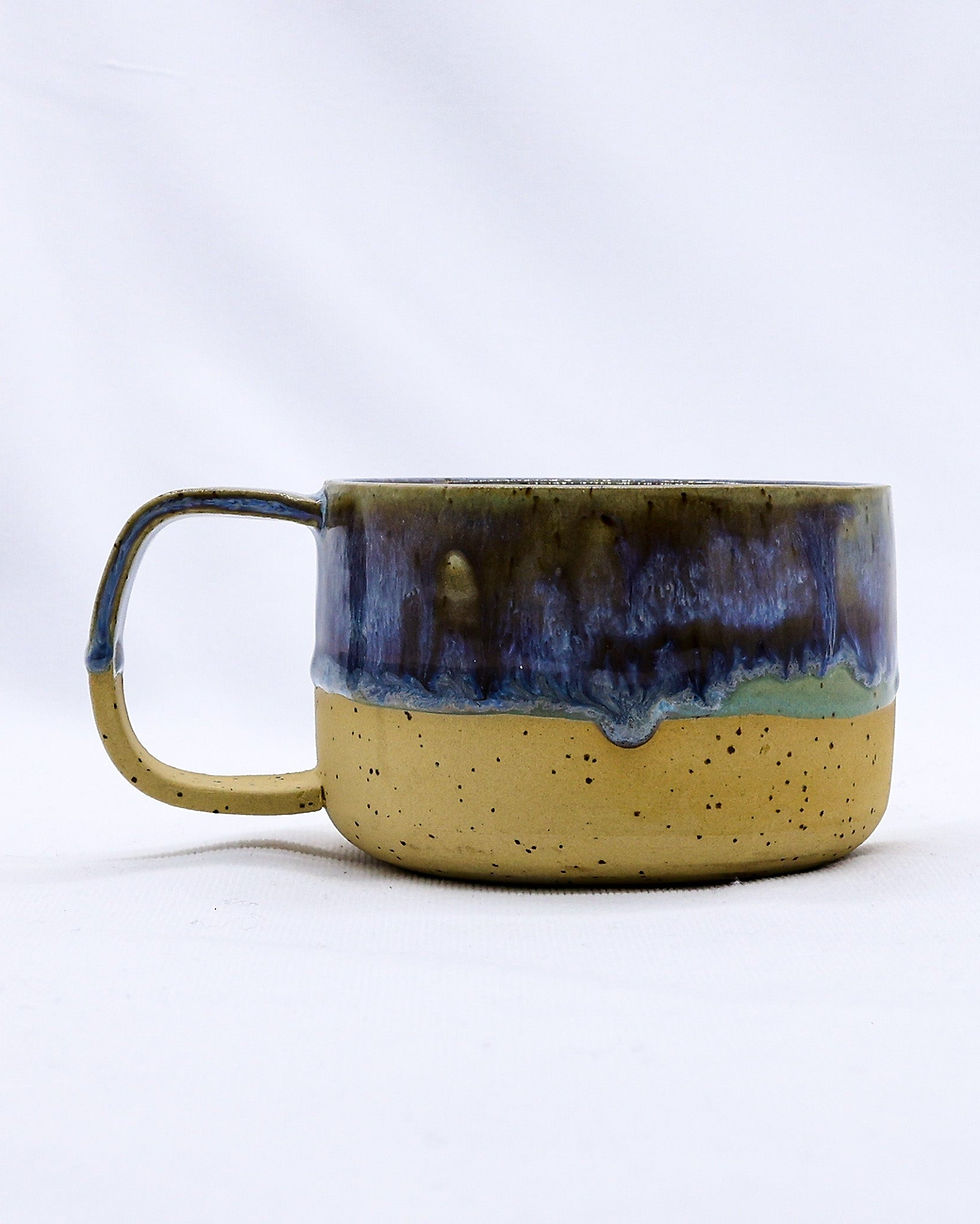 Handmade ceramic mug with blue drip glaze over speckled tan