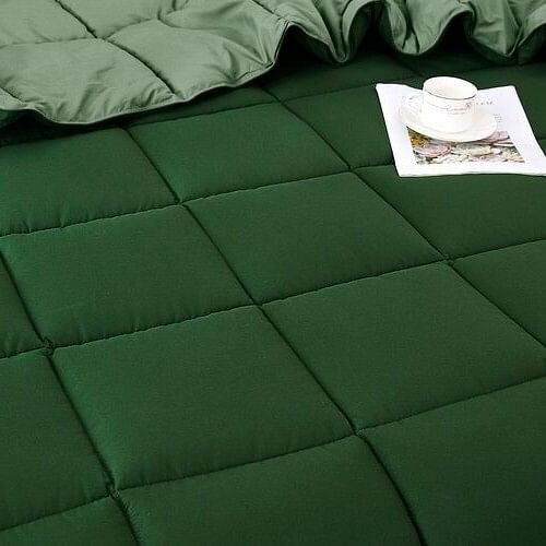 Dark green quilted blanket with a white cup and magazine on top