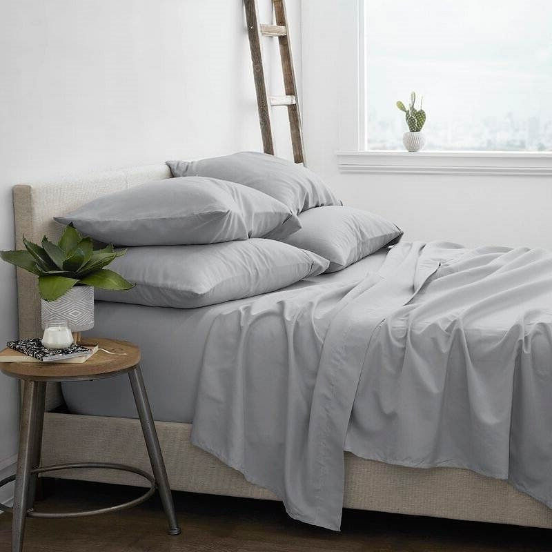 Bed with light grey bedding, pillows, and a side table