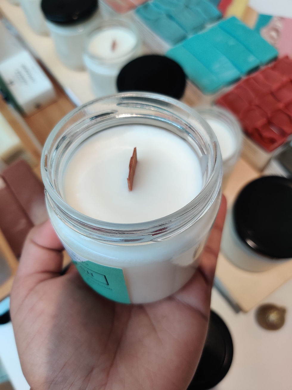 Hand holding a white candle with a wooden wick