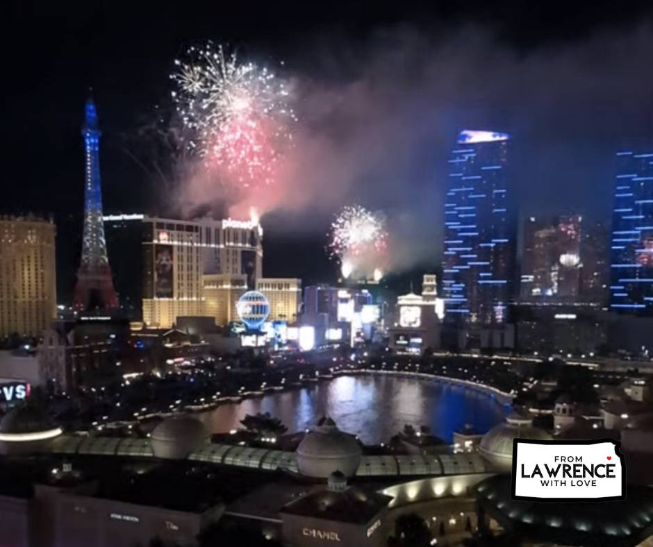 Fireworks light up the night sky over a brightly lit cityscape with a replica Eiffel Tower. Text reads “From Lawrence with Love.”