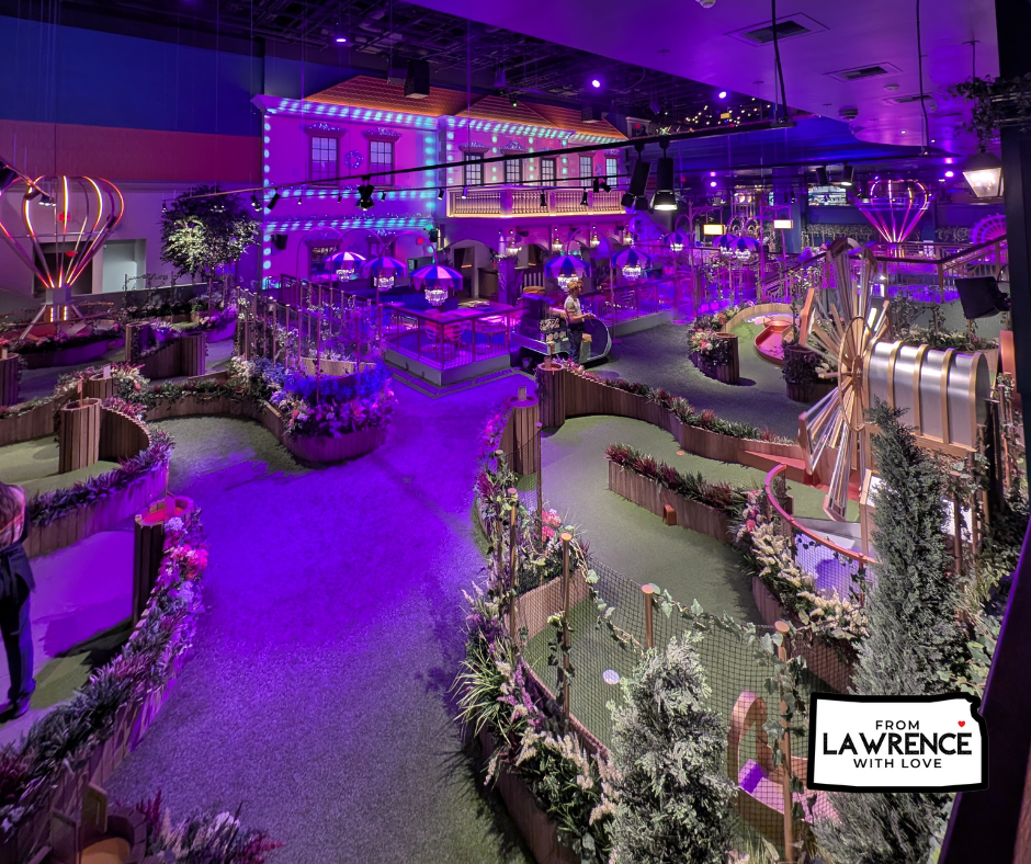 Vibrant indoor mini-golf course with purple lighting, decorative plants, and a Ferris wheel. "From Lawrence with Love" text is visible.